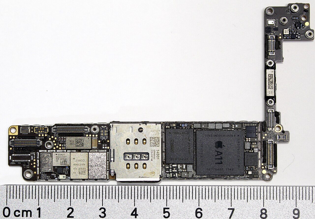 An iPhone 8 main logic board beside a centimetre ruler, with the A11 chip, marked with the Apple logo, in the middle