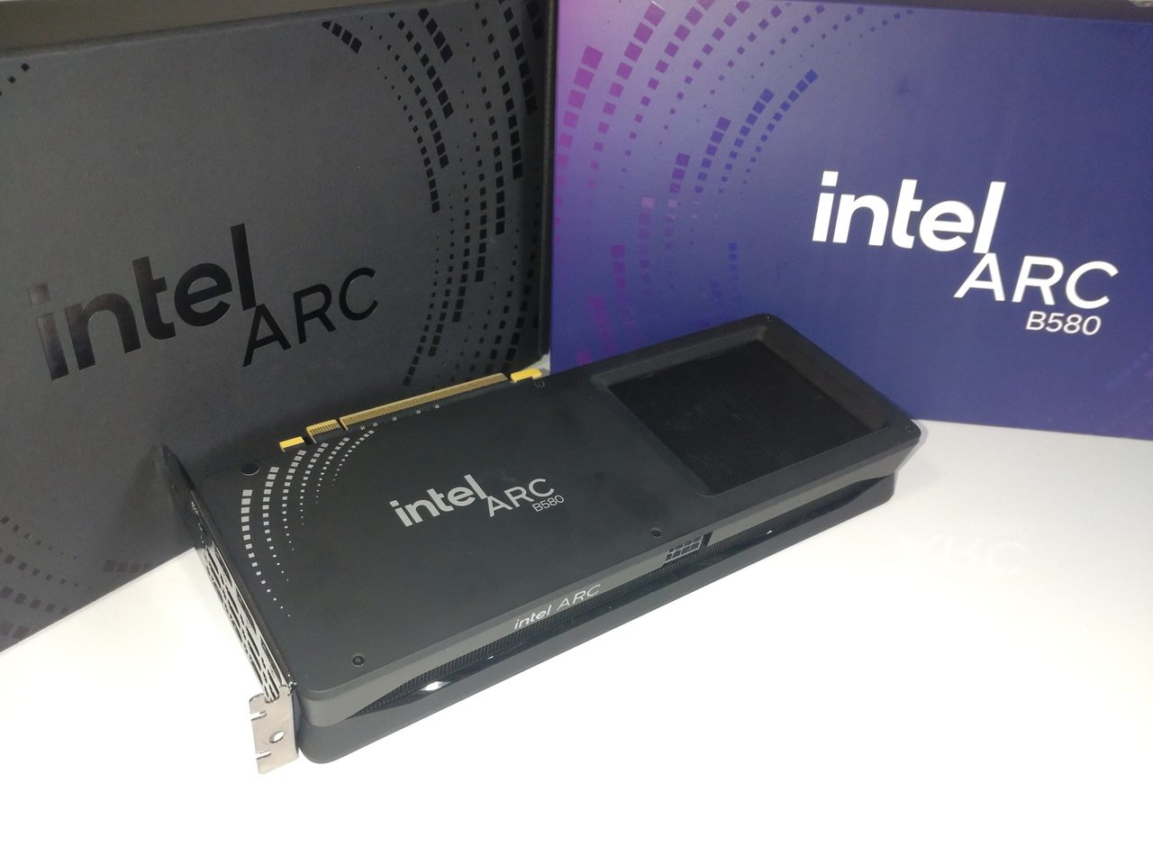 An Intel Arc B580 Limited Edition graphics card lying in front of its box, a black card with a dotted pattern and the Intel Arc logo, the box printed with Intel Arc B580 in white on dark blue