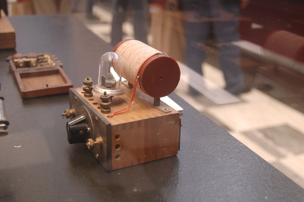 A small homemade radio on a wooden base: a coil of wire, brass terminals, and a glass dome covering a crystal and a fine wire