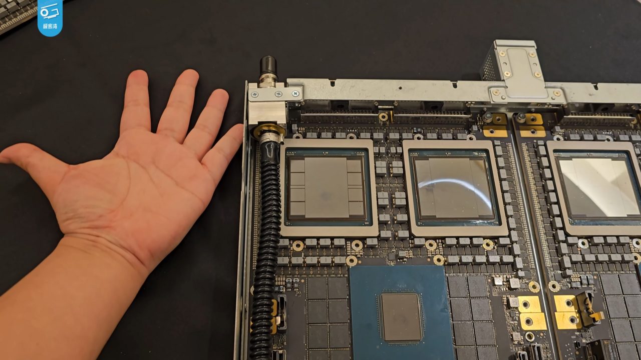 A hand laid flat beside a GB200 compute board, with three large square GPU packages in a row and a smaller CPU package below them