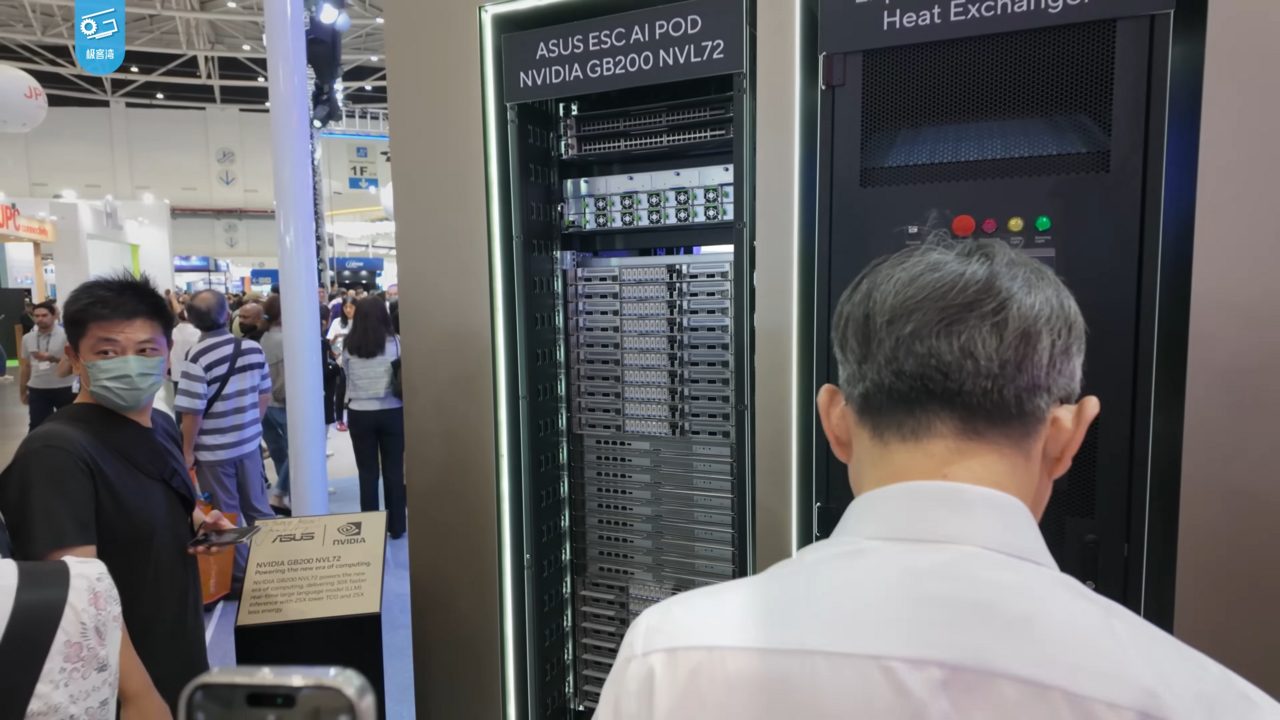 Visitors at a trade show beside a tall black server rack labelled ASUS ESC AI POD NVIDIA GB200 NVL72, its trays visible through the front, next to a unit labelled Heat Exchanger
