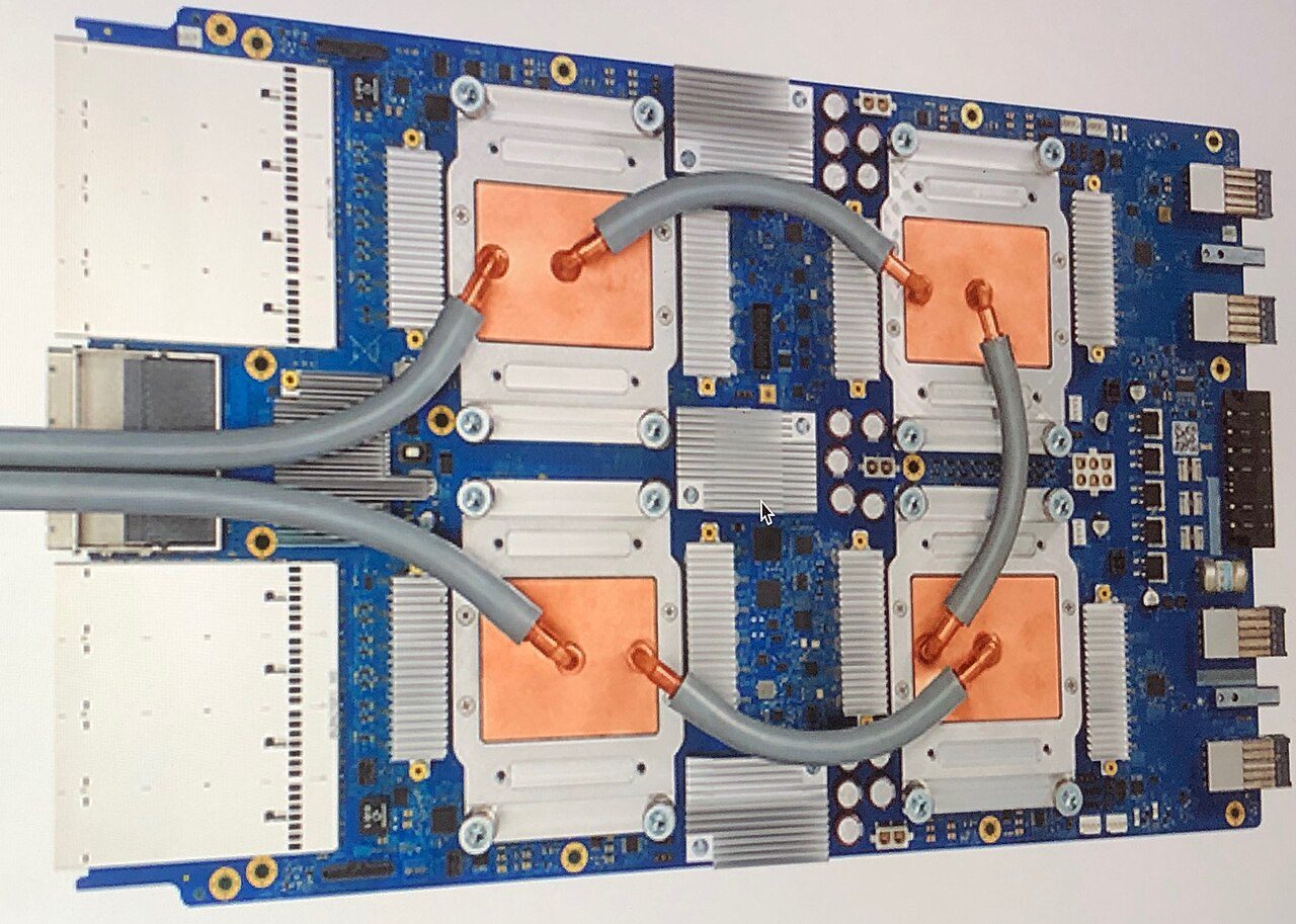 A Google TPU v3 board with four chips under copper cold plates joined by grey coolant tubes, with heatsinks and network connectors around the edges