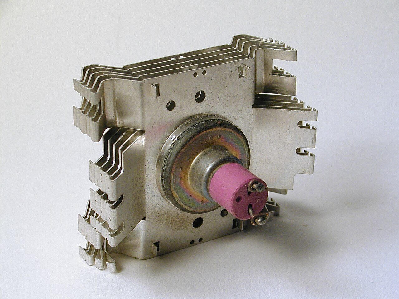 A magnetron taken out of a microwave oven: a metal block with cooling fins on either side and a pink ceramic cylinder with two screw terminals at the front