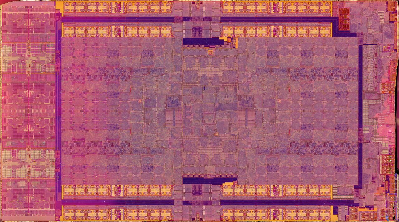 Die photograph of the PlayStation 5 processor in pink, orange and purple tones: a wide rectangular chip covered in blocks of repeated structure, with rows of interface circuitry along its long edges