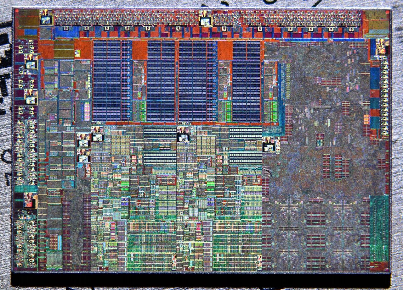 A colour-enhanced die photograph showing a dense, regular grid of circuit blocks in blue, red, green and grey, with arrays of identical rectangular structures across the upper half