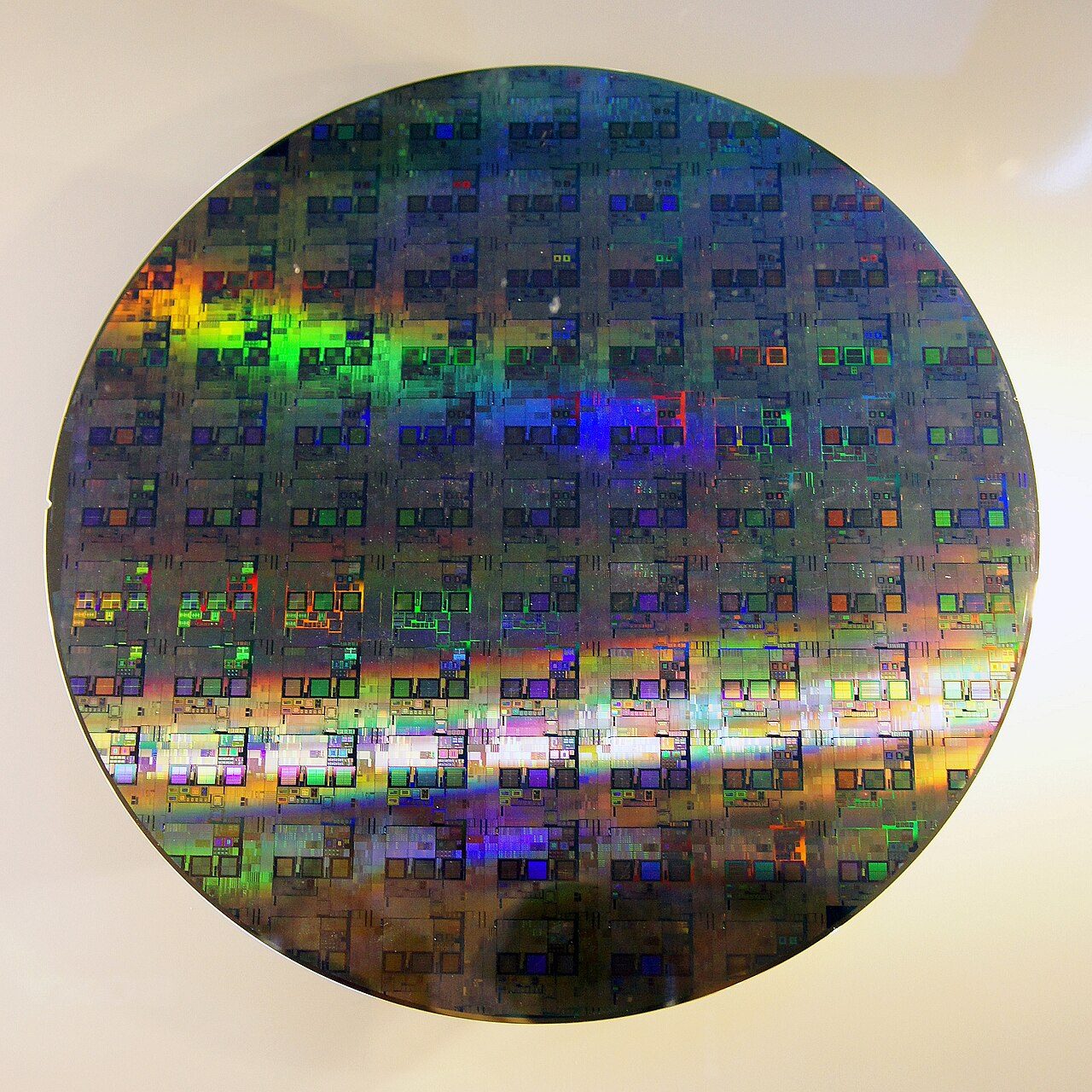 A 300 mm silicon wafer covered in a grid of identical rectangular chips, shimmering with rainbow colours